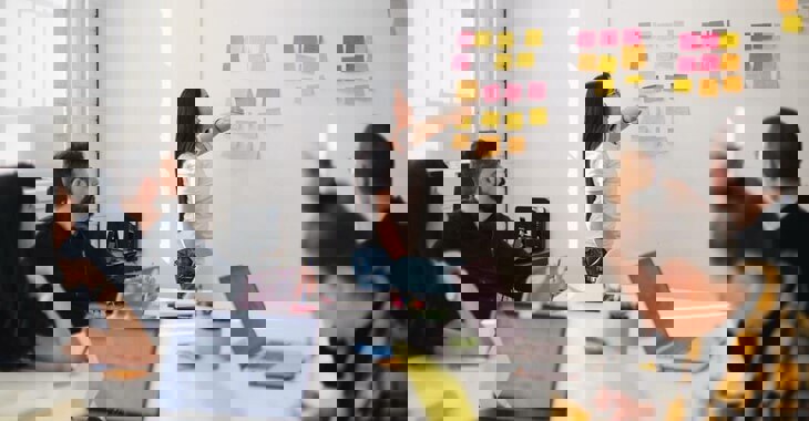 Woman Presenting At A Post It Note Wall In A Group Office Setting