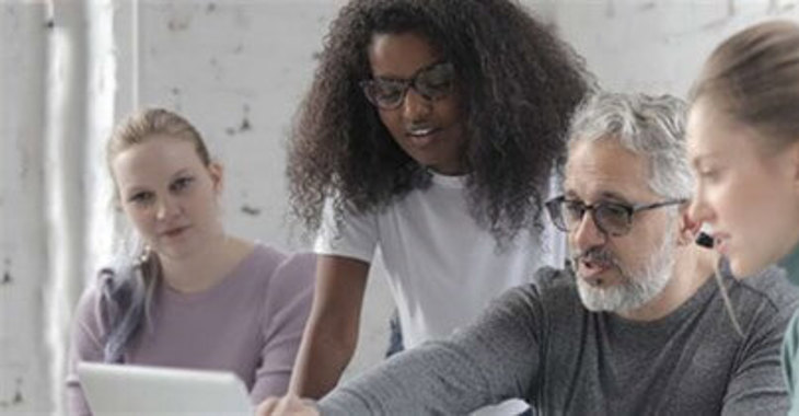 Four People Gathered Around A Laptop 