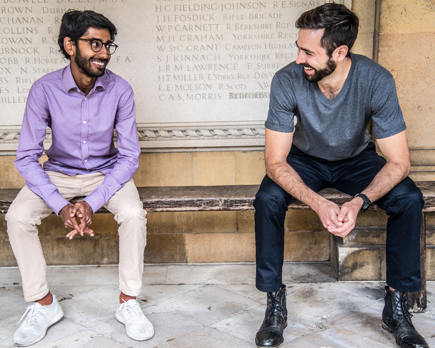 Dr Ravi Solanki and Raymond Siems, volunteers for the charity HEROES, are sitting on a bench, they are both smiling.